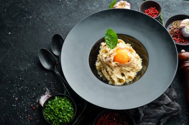 Yumurtalı, parmesan peynirli ve siyah taşlı bir tabakta fesleğenli Carbonara makarnası. Üst Manzara. Kırsal biçim.
