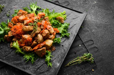 Siyah taş bir tabakta bira içinde sebzelerle pişirilmiş domuz eti. Üst Manzara. Siyah bir arkaplanda.