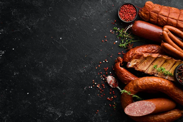 Biberiyeli sosis, salam ve tütsülenmiş et seti ve siyah bir taş zemin üzerinde baharatlar. Üst Manzara. Metin için boş alan.