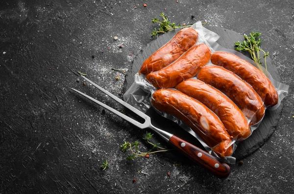 Smoked sausages in vacuum packaging. Top view. On a black background.