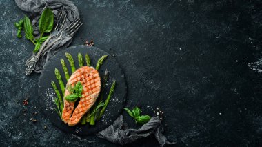 Pişmiş kuşkonmaz ve siyah taş tabakta baharatlı somon bifteği. Üst Manzara. Metnin için boş yer.