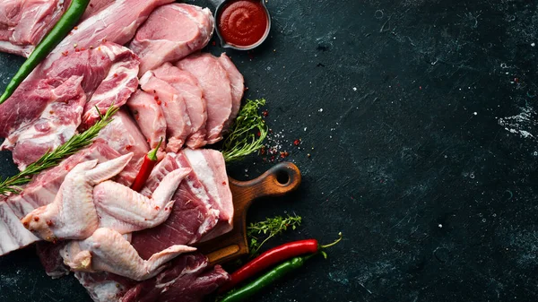 Raw meat background. Meat on a black stone background with spices and herbs. Top view. Rustic style.