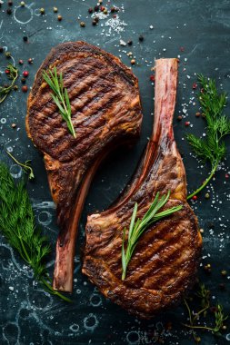 Kemiğe baharat ve otlarla birlikte iki biftek. Siyah taştan bir arka planda. Üst Manzara. Boş kopyalama alanı.