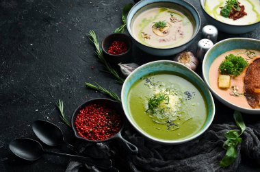 Siyah taşlı arka planda, kâselerdeki renkli çorbalar. Sağlıklı yiyecekler. Üst Manzara. Kırsal biçim.