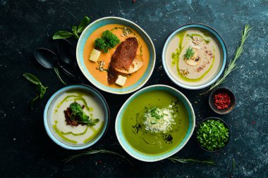 Siyah taşlı arka planda, kâselerdeki renkli çorbalar. Sağlıklı yiyecekler. Üst Manzara. Kırsal biçim.