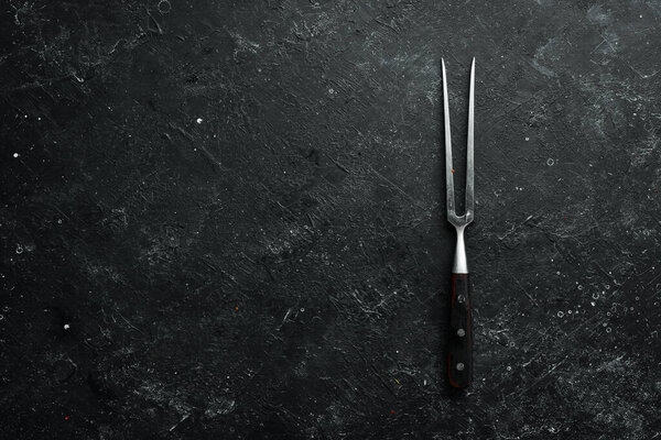 Вилка для стейка на черном каменном фоне. Вид сверху. Сельский стиль.