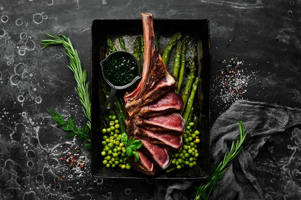Tomahawk steak on the bone. Grilled steak with asparagus and green peas. On a black background. Top view. Free copy space.