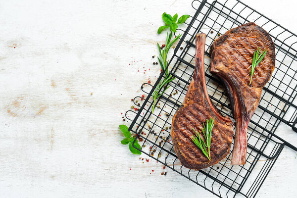 Tamahavk steak on the bone with spices and herbs. On a white wooden background. Top view. Free copy space.