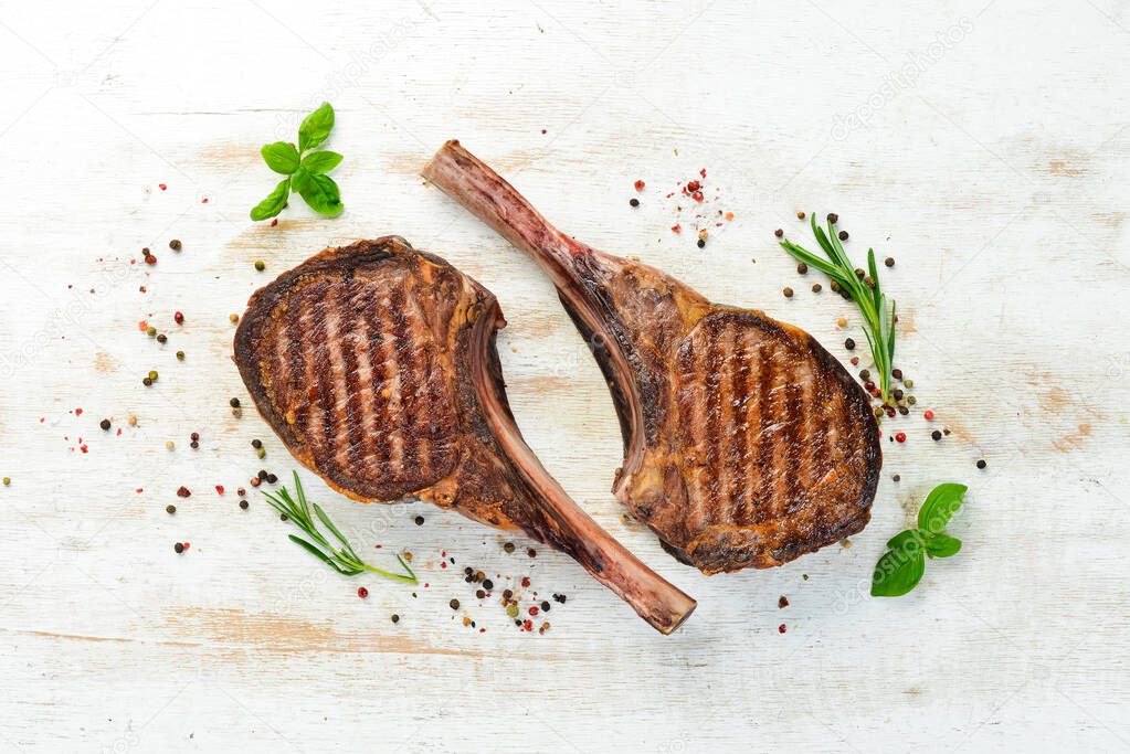 Tamahavk steak on the bone with spices and herbs. On a white wooden background. Top view. Free copy space.