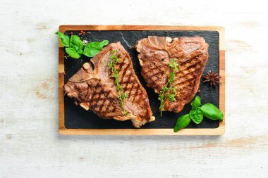 Grilled aged T-bone steak with rosemary on a white wooden background. Top view. Rustic style. clipart