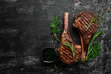Kemiğe baharat ve otlarla birlikte iki biftek. Siyah taştan bir arka planda. Üst Manzara. Boş kopyalama alanı.