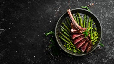 Kemiklerde Tomahawk bifteği. Kuşkonmaz ve bezelyeli ızgara biftek. Siyah bir arka planda. Üst Manzara. Boş kopyalama alanı.