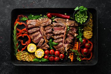 Kemiğin üzerinde biftek ve metal bir tencerede ızgara sebze. Üst Manzara. Kırsal biçim.