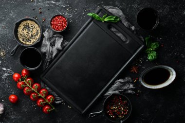 Siyah taş mutfak arka planı. Baharatlı siyah bir masanın üzerinde ahşap mutfak tahtası. Üst Manzara. Kırsal biçim.