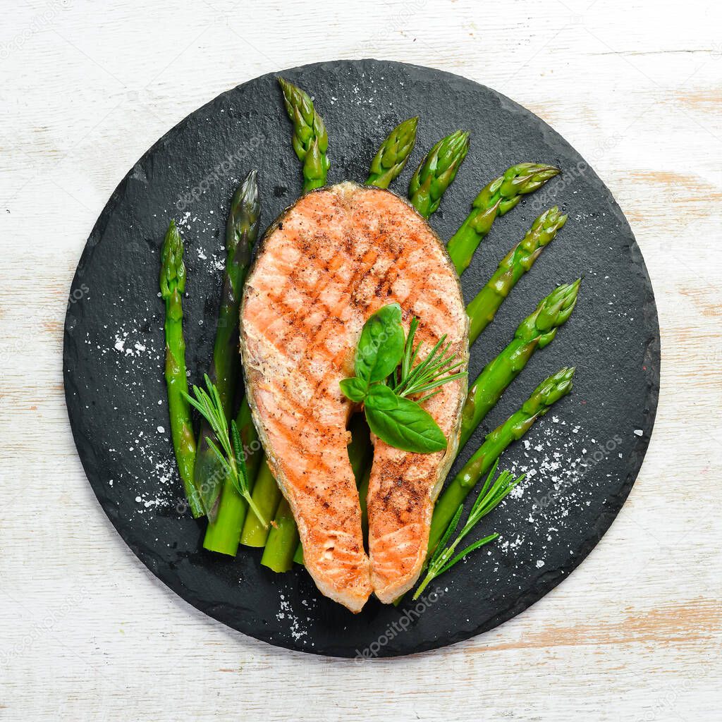 Salmon steak with baked asparagus and spices on a black stone plate. Top view. Free space for your text.