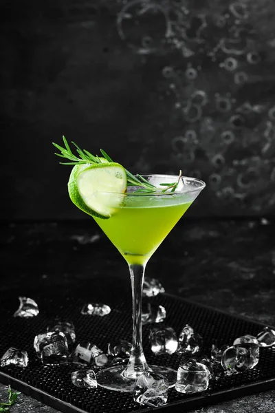 Green alcoholic cocktail with lime and rosemary. On a black stone background. Menu bar.