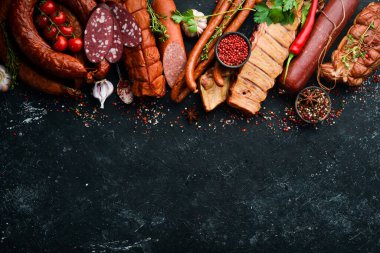 Biberiyeli sosis, salam ve tütsülenmiş et seti ve siyah bir taş zemin üzerinde baharatlar. Üst Manzara. Metin için boş alan.