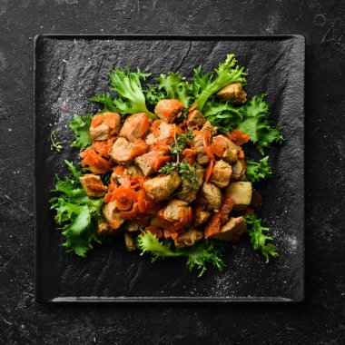 Siyah taş bir tabakta bira içinde sebzelerle pişirilmiş domuz eti. Üst Manzara. Siyah bir arkaplanda.