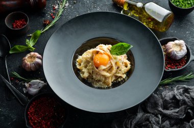 Yumurtalı, parmesan peynirli ve siyah taşlı bir tabakta fesleğenli Carbonara makarnası. Üst Manzara. Kırsal biçim.