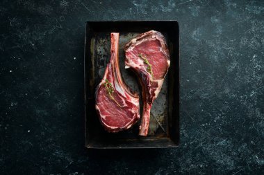 Kemiğe baharatlı iki çiğ biftek. Siyah taştan bir arka planda. Üst Manzara. Boş kopyalama alanı.