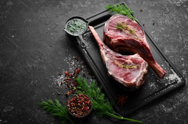Kemiğe baharatlı iki çiğ biftek. Siyah taştan bir arka planda. Üst Manzara. Boş kopyalama alanı.