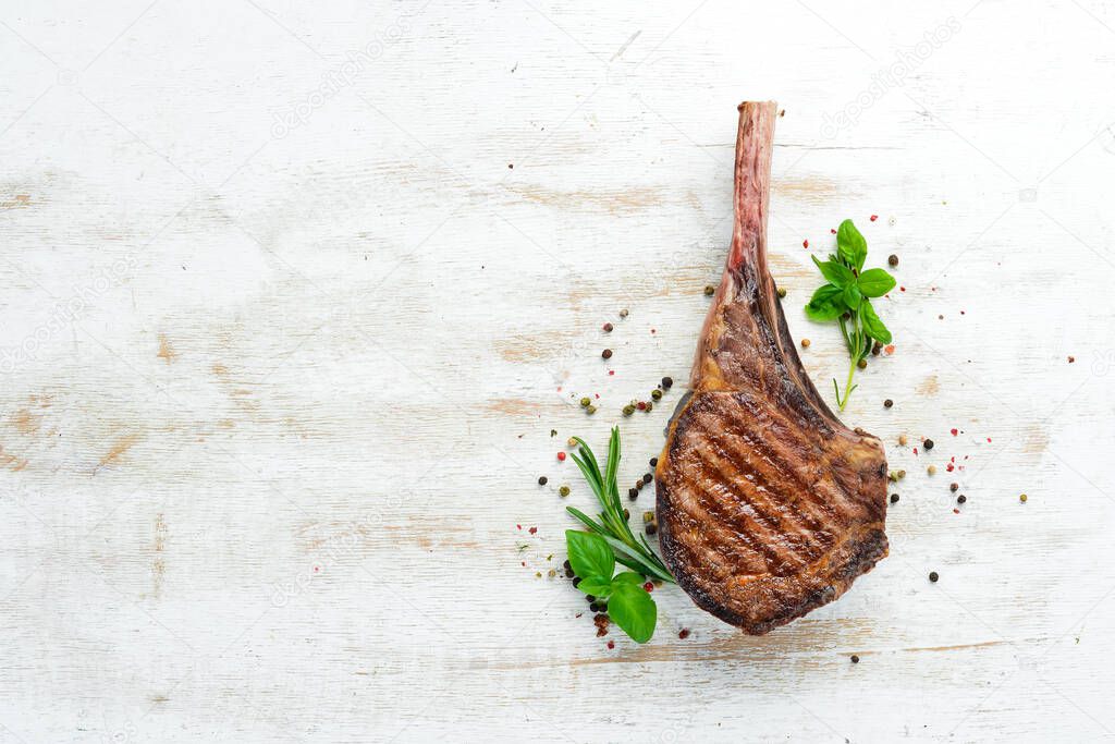 Tamahavk steak on the bone with spices and herbs. On a white wooden background. Top view. Free copy space.