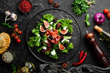 Jambonlu salata, böğürtlen, incir ve peynir. Siyah taştan bir tabakta. Sağlıklı yiyecekler. Üst görünüm.