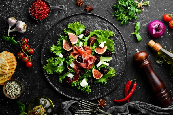 Jambonlu salata, böğürtlen, incir ve peynir. Siyah taştan bir tabakta. Sağlıklı yiyecekler. Üst görünüm.