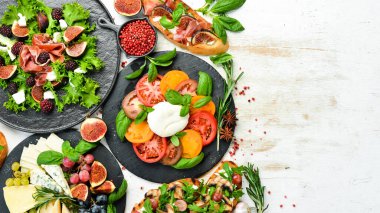 Tabaklardaki yiyecekler: peynir, incir, makarna ve etli mantar. Beyaz ahşap arka planda sağlıklı yiyecekler. Üst görünüm.