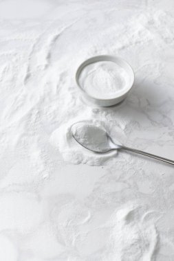 Baking soda in a bowl and in a spoon on the marble countertop clipart