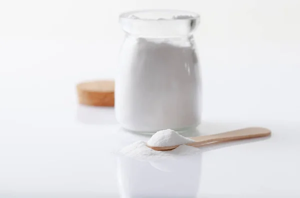 Bicarbonato de sodio en un frasco y una cuchara de madera sobre una mesa blanca brillante —  Fotos de Stock
