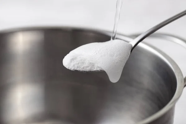 Mengocok baking soda dengan cuka dalam sendok di atas piring logam — Stok Foto