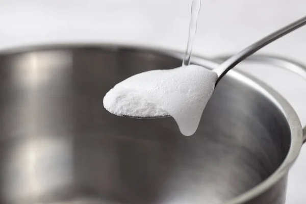 Espuma de bicarbonato de sodio saciado con vinagre en una cuchara sobre un plato de metal —  Fotos de Stock