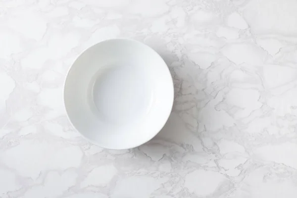 A white bowl on a marble surface. Overhand. — Stock Photo, Image