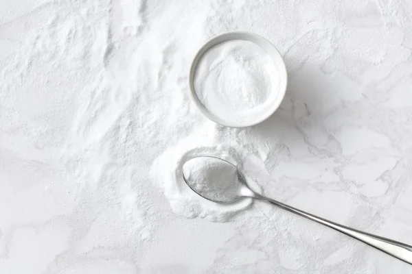 Baking soda in a bowl and in a spoon on the marble countertop