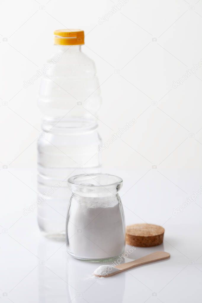 A jar of baking soda and a bottle of vinegar on a white table