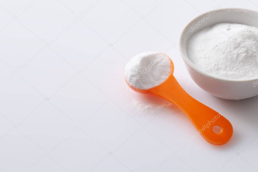 Measuring spoon with artificial sweetener aspartame E951 and a bowl of blemish on a white glossy background
