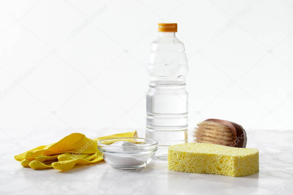 Baking soda, a bottle of vinegar, rubber gloves on a marble surface.