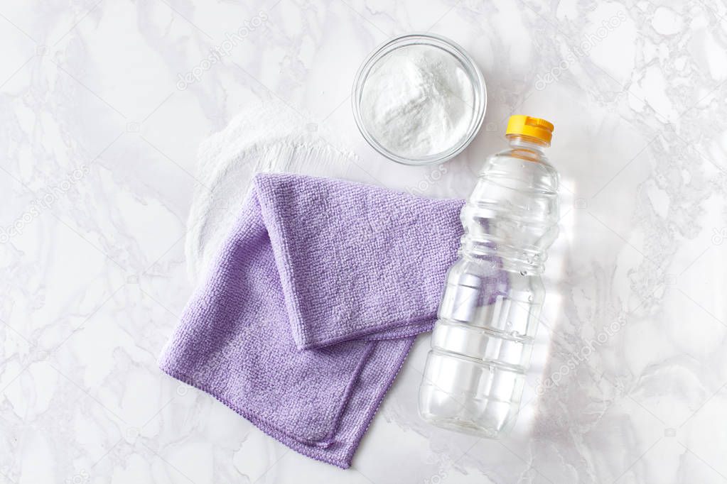 Vinegar in a bottle, baking soda and a cleaning cloth on a marble surface
