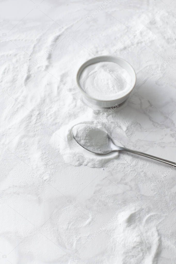 Baking soda in a bowl and in a spoon on the marble countertop