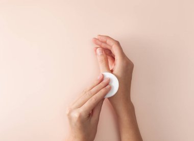 Kadın elleri pembe bir arka planda pamuklu bir eli siliyor.