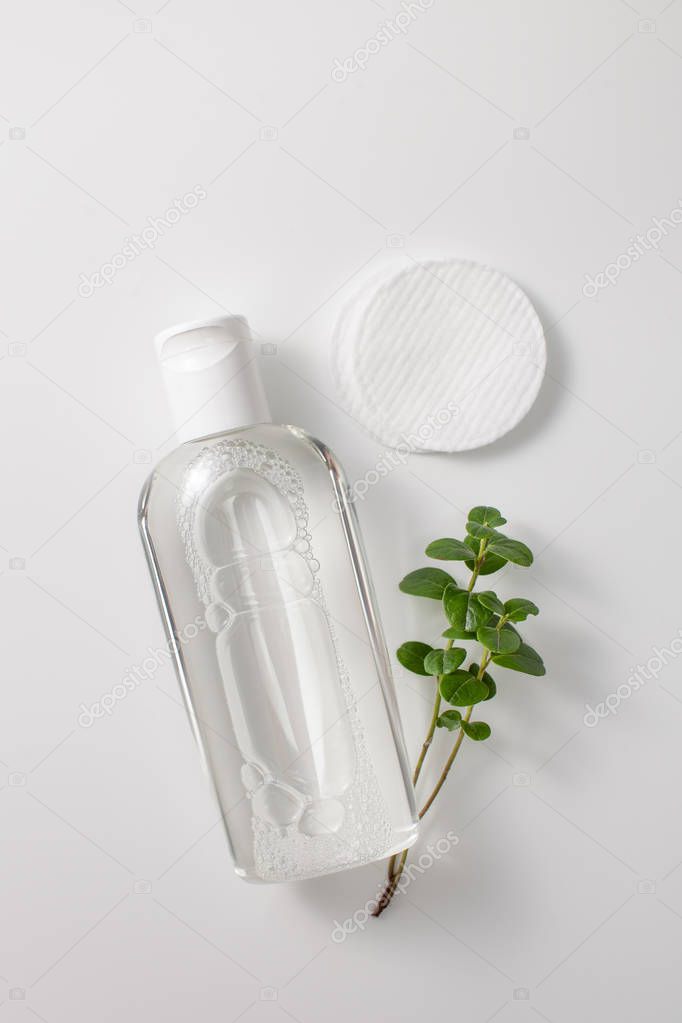 Micellar cleansing water in a bottle, cotton pads and a sprig of greenery