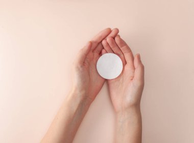 Kadınların açık avuçlarında pembe bir arka planda pamuk pedi