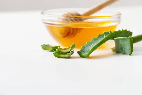 Hojas de aloe vera y miel fresca en un bol sobre fondo blanco — Foto de Stock
