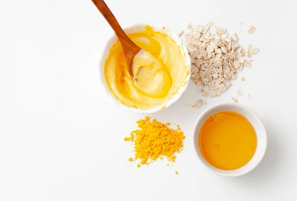 Preparation a rejuvenating homemade face mask made of turmeric, honey and oatmeal on a white background. Copy space text.