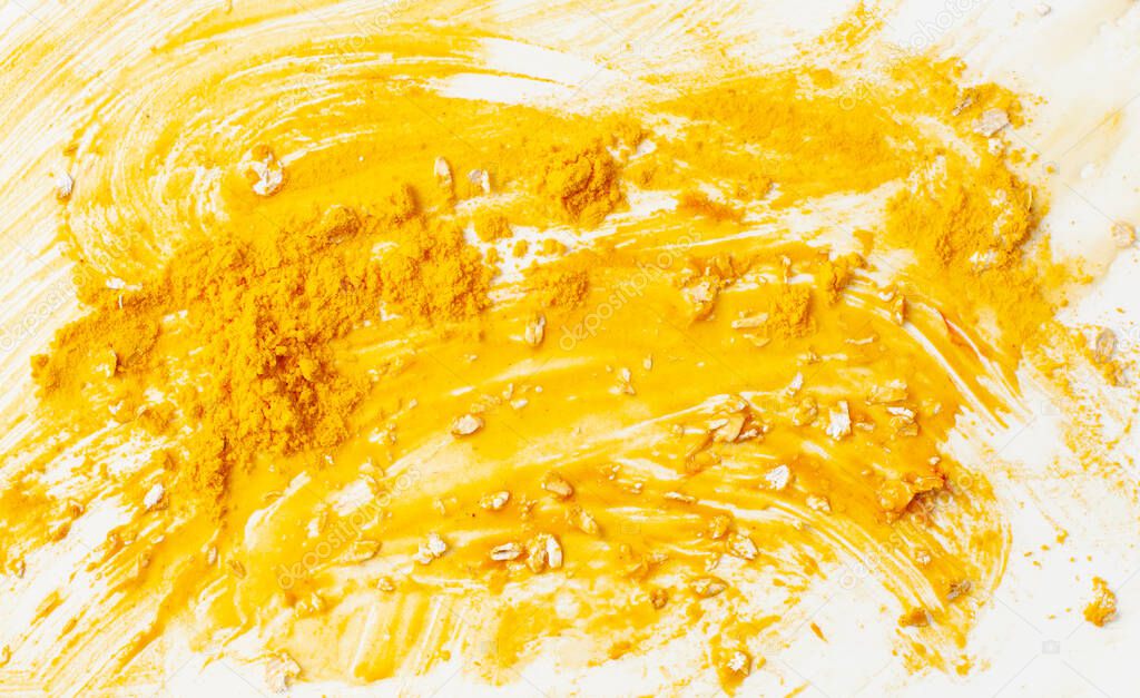 Bright yellow aromatic spice turmeric for health and beauty. Texture background of a smeared face mask made of turmeric, honey and oatmeal on a white. Copy space text.