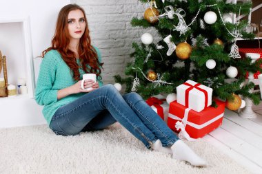 Gülümseyen genç kadın güzel Noel ağacı evde yakınındaki bir hediye kutusu açılıyor. Lüks Noel dekorasyonu. Noel ve yeni yıl hediye.