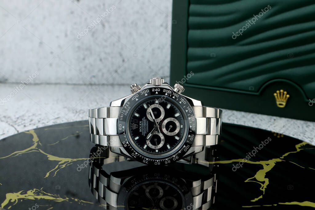 Rolex wristwatch model cosmograph daytona oyster perpetual superlative chronometer with black ceramic bezel stainless steel body on stone table with cement wall background in authorized luxury shop