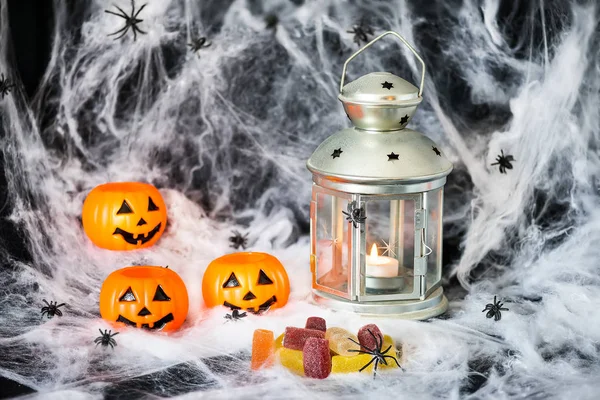halloween pumpkins with candies and lit lamp with a candle on background of cobwebs