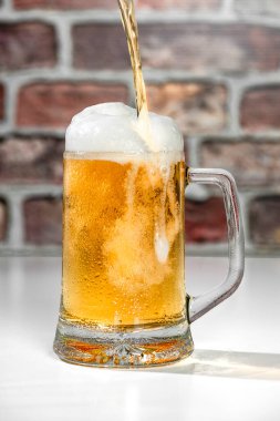 Beyaz bardakta köpüklü, kırmızı tuğlalı arka planda serinletici bir bira bardağı servis ediyorum.